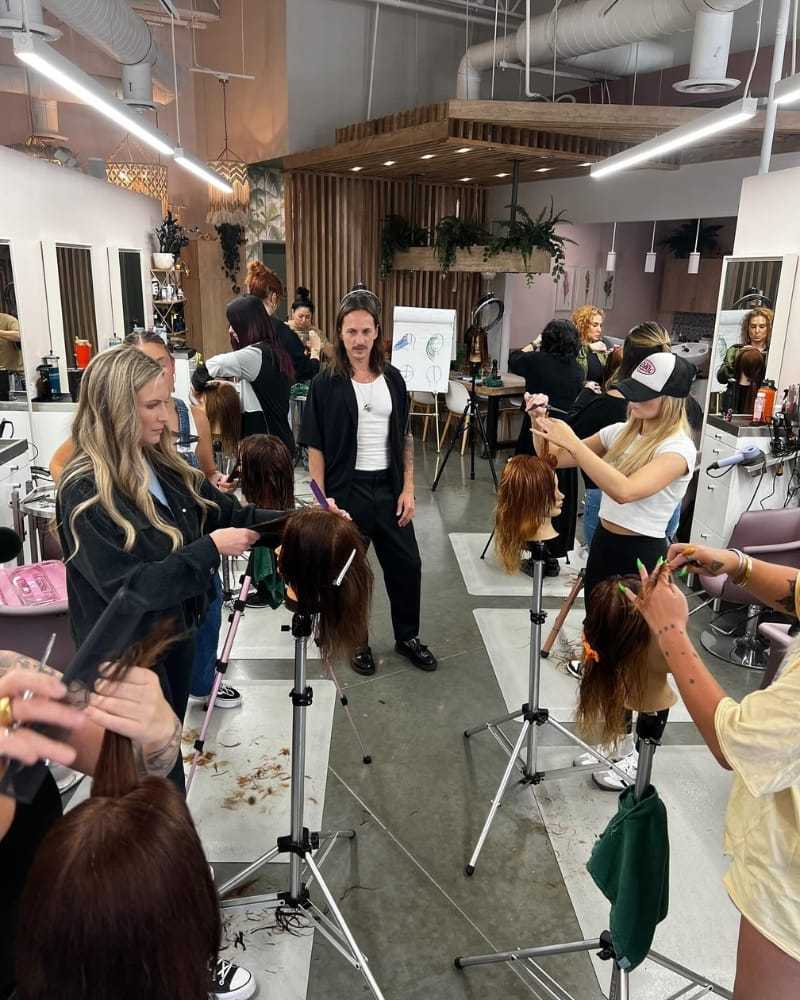 Stylists practicing haircuts on mannequins in a salon setting.