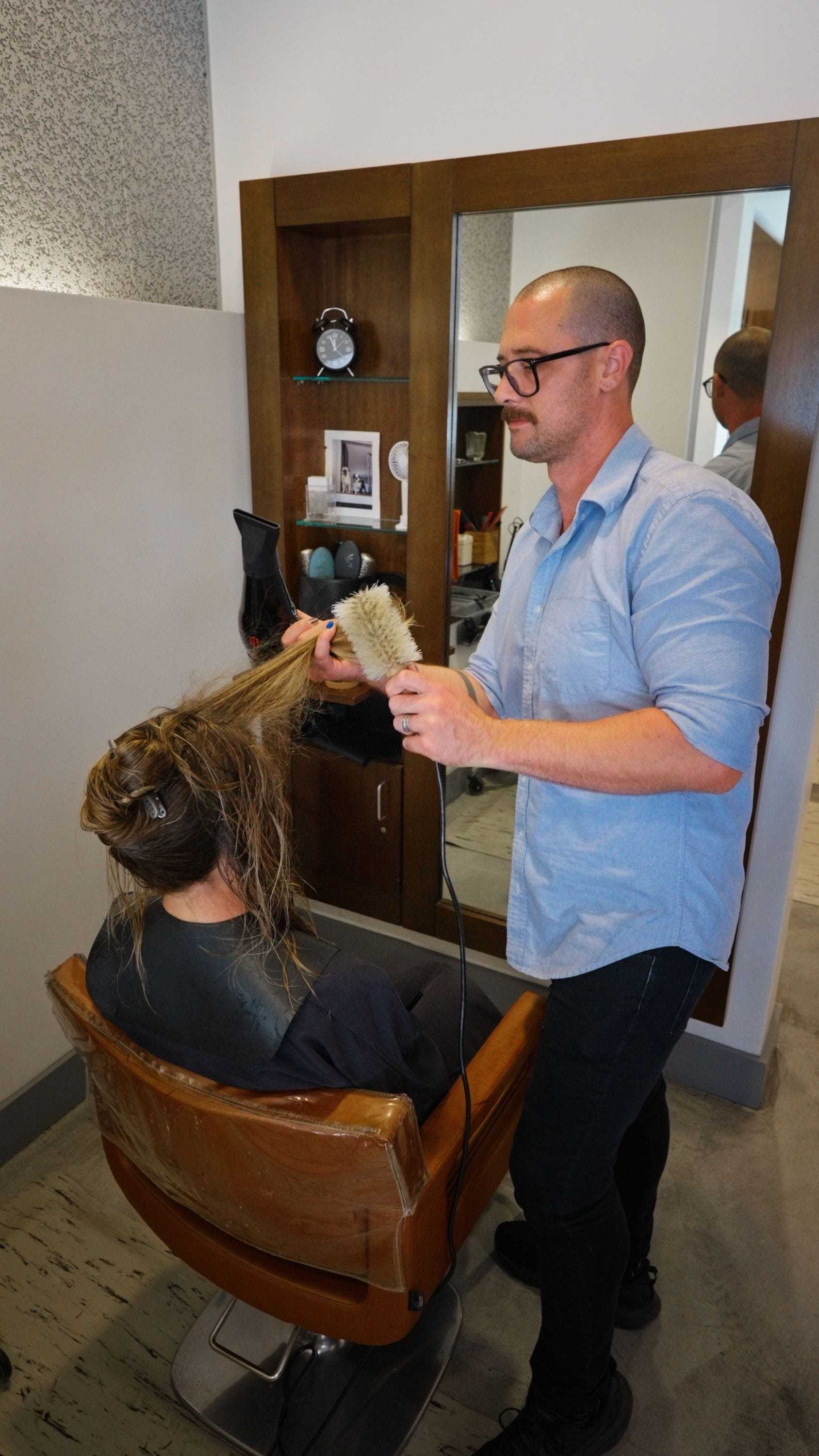 Hairstylist blow-drying a client's hair in a salon.