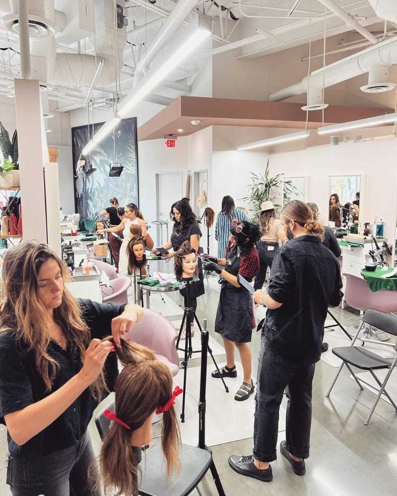 Hairdressing students practice styling on mannequins in a bright, modern salon classroom.