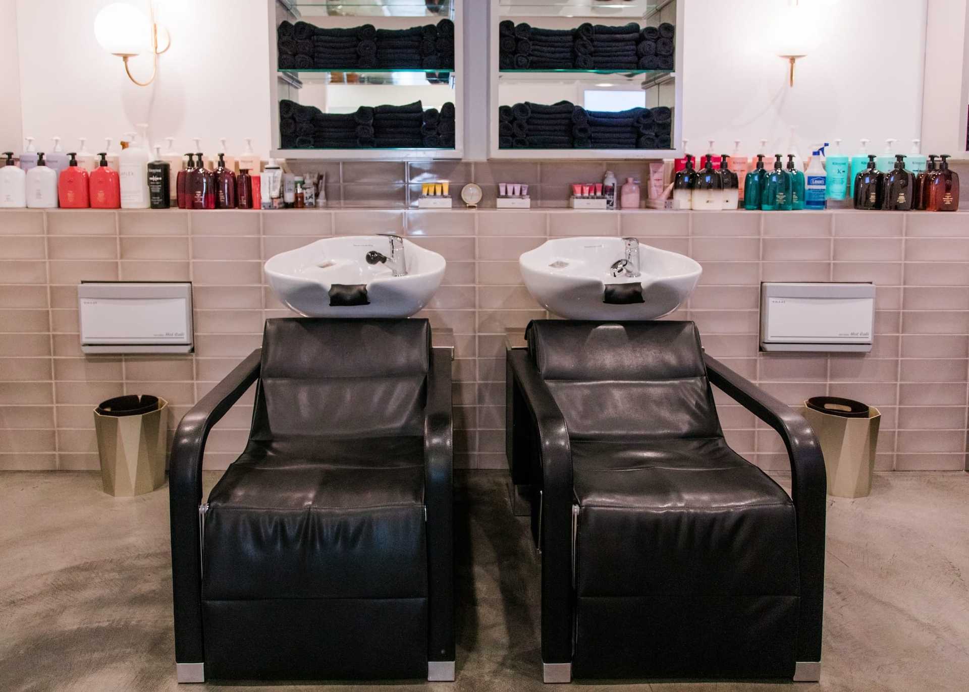Two black salon chairs with sinks in a modern hair salon setting.