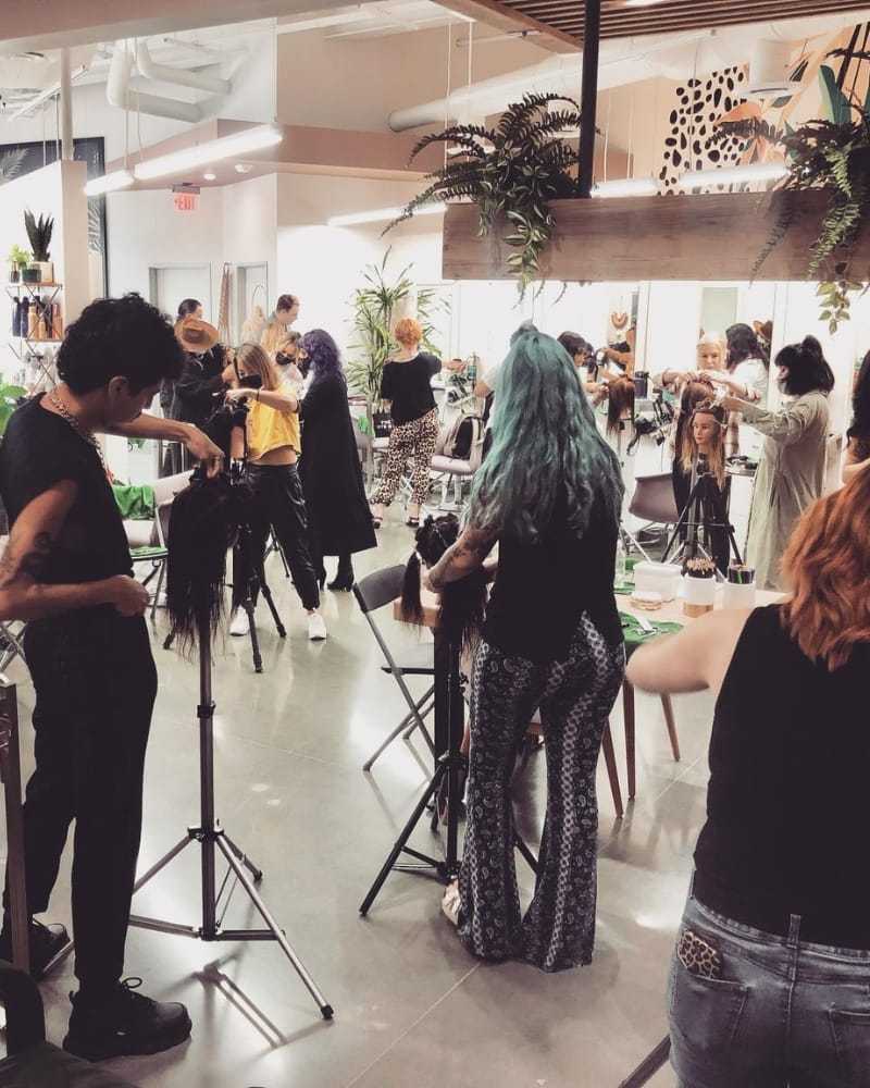 Modern salon with stylists working on clients' hair amid lively, bustling atmosphere.