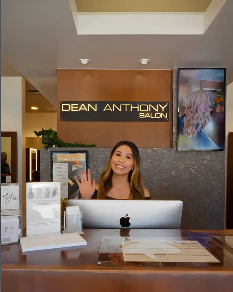 Receptionist smiling at the front desk of Dean Anthony Salon with salon decor.