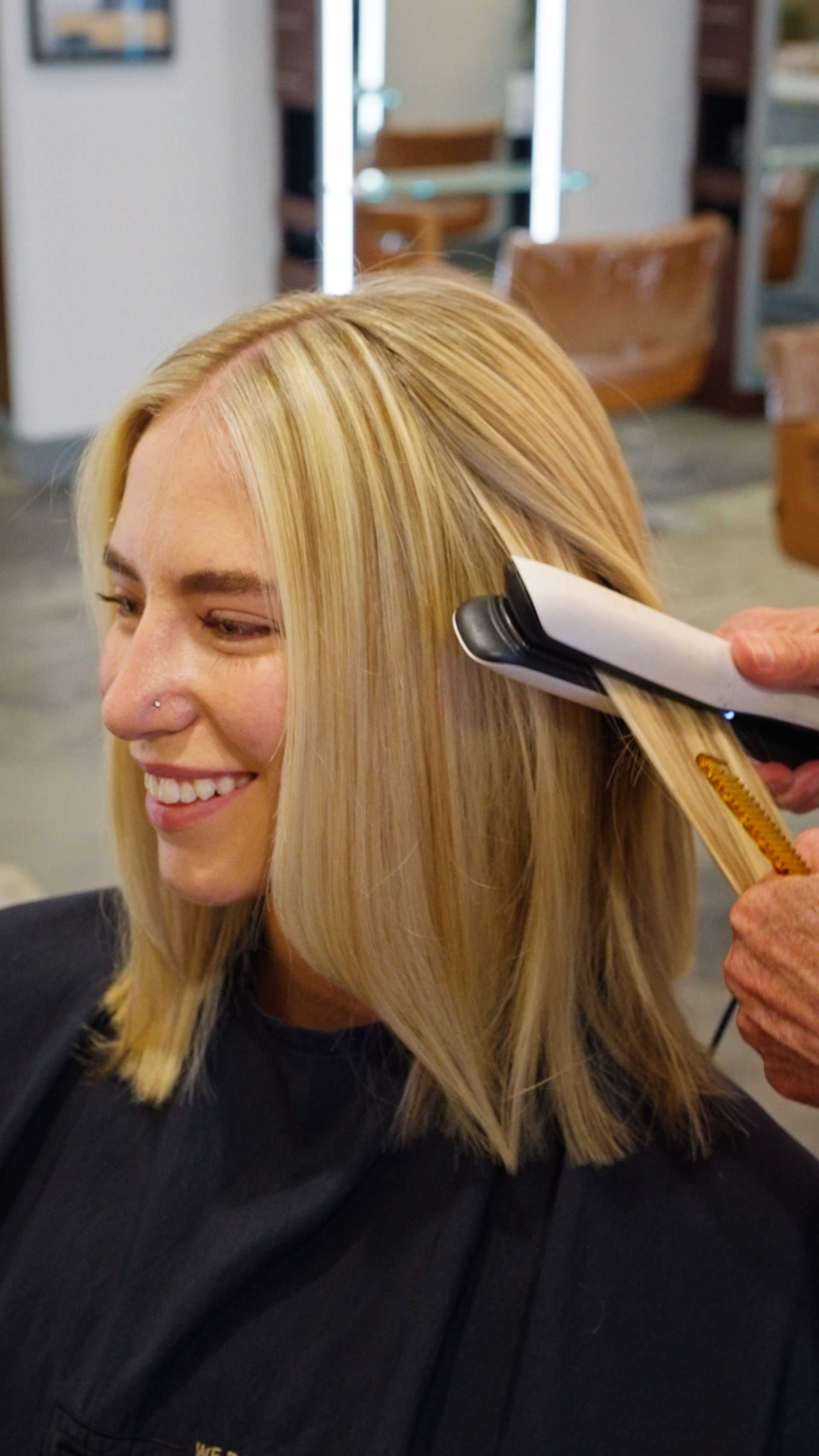 Woman with blonde hair getting hair styled with a straightener in a salon.